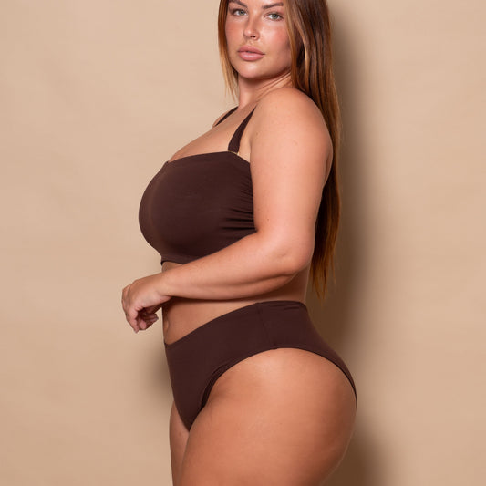 plussize woman wearing a chocolate brown bikini set against a beige background