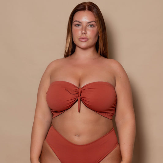 plussize woman wearing a rust red bikini set against a beige background
