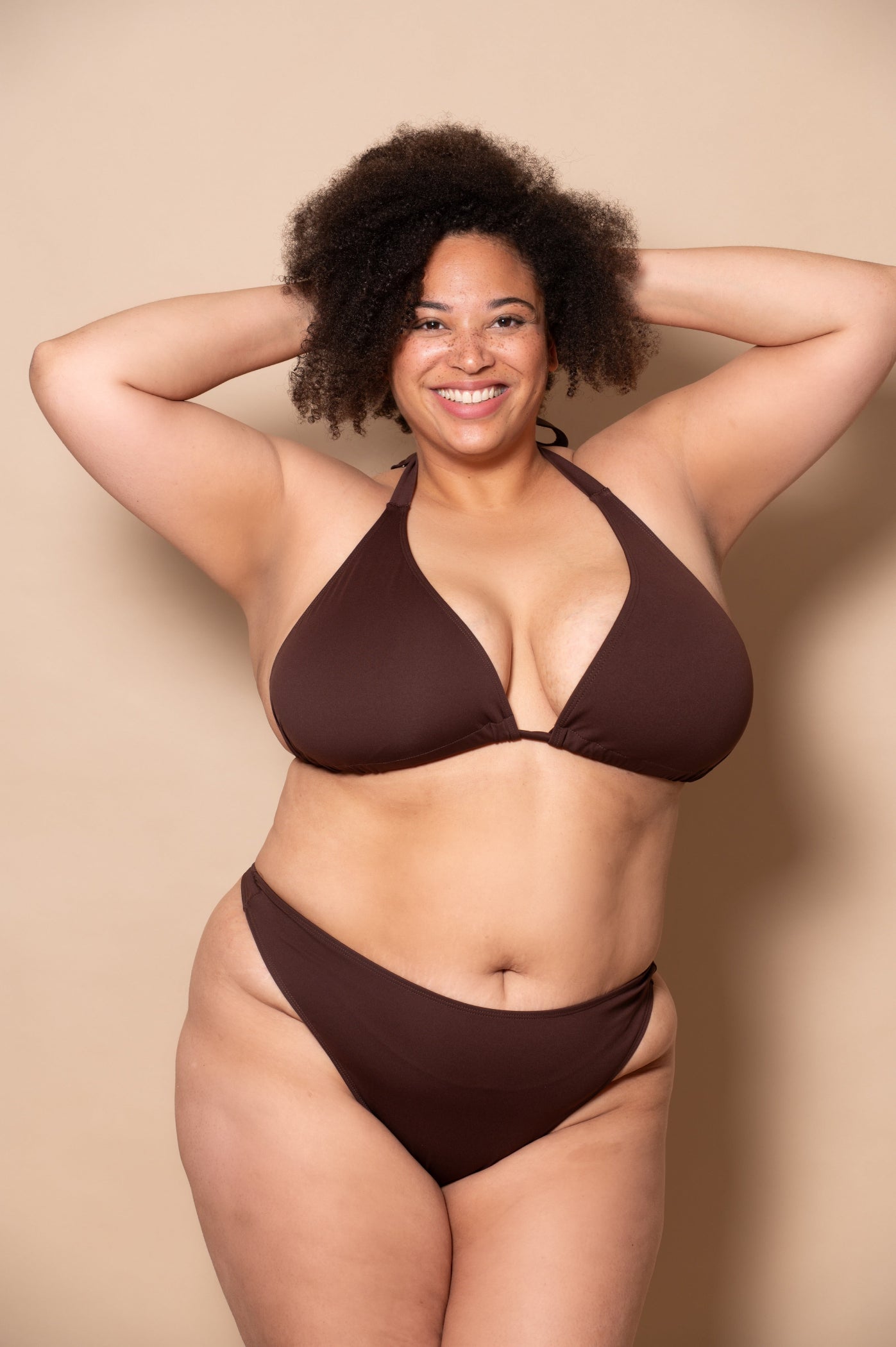 plussize woman wearing a chocolate brown bikini set against a beige background