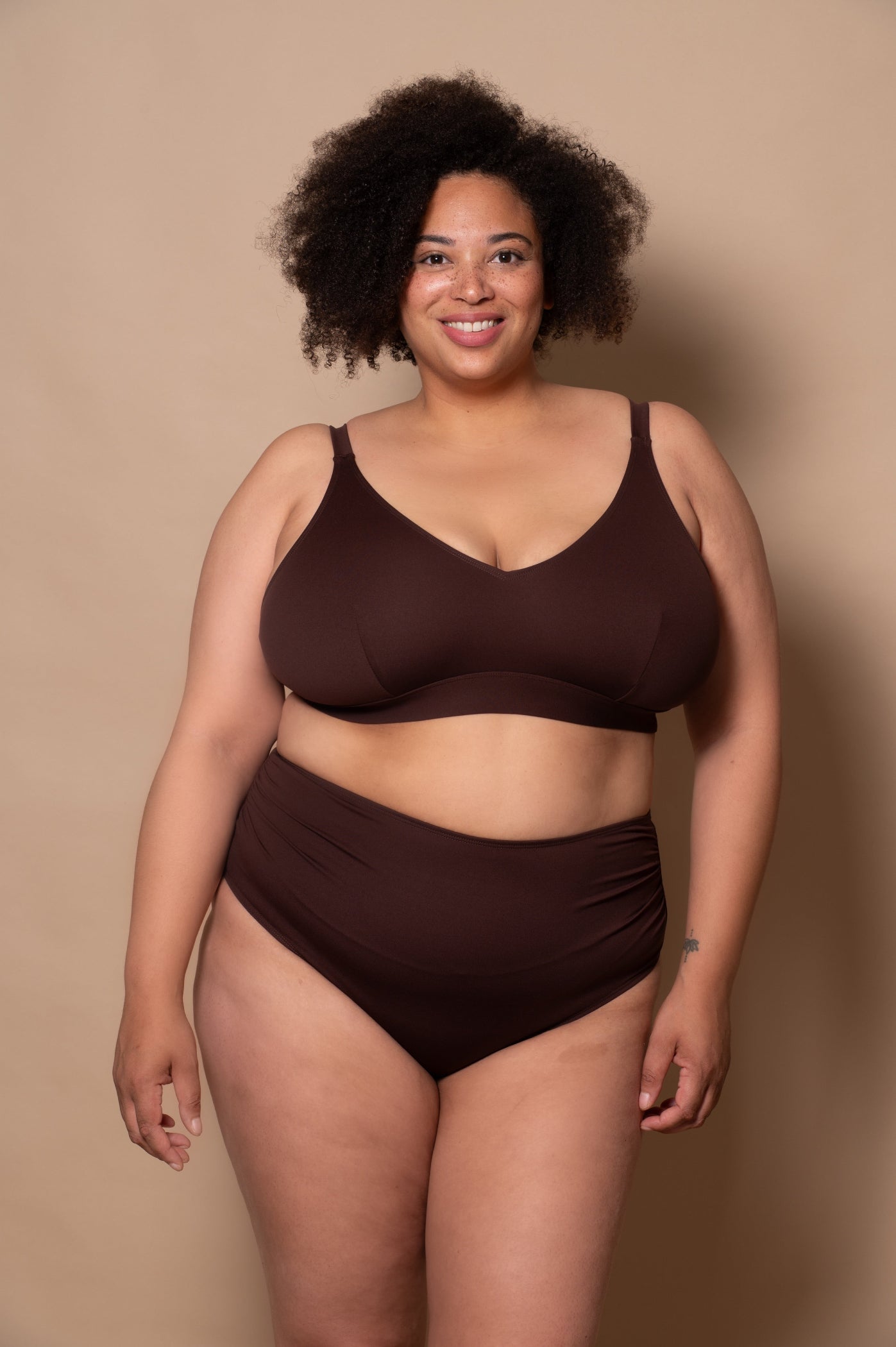plussize woman wearing a chocolate brown bikini against a beige background