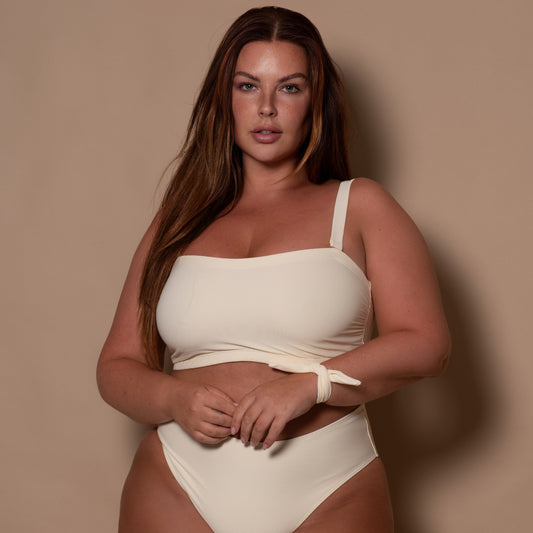 plussize woman wearing a cream white bikini against a beige background