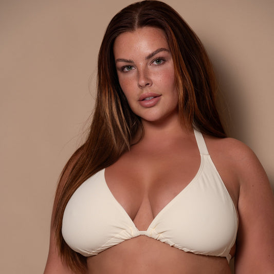 plussize woman wearing a cream white bikini against a beige background