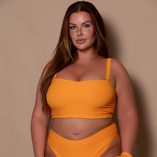 curvy woman wearing a yellow ribbed bikini bandeau against a beige background