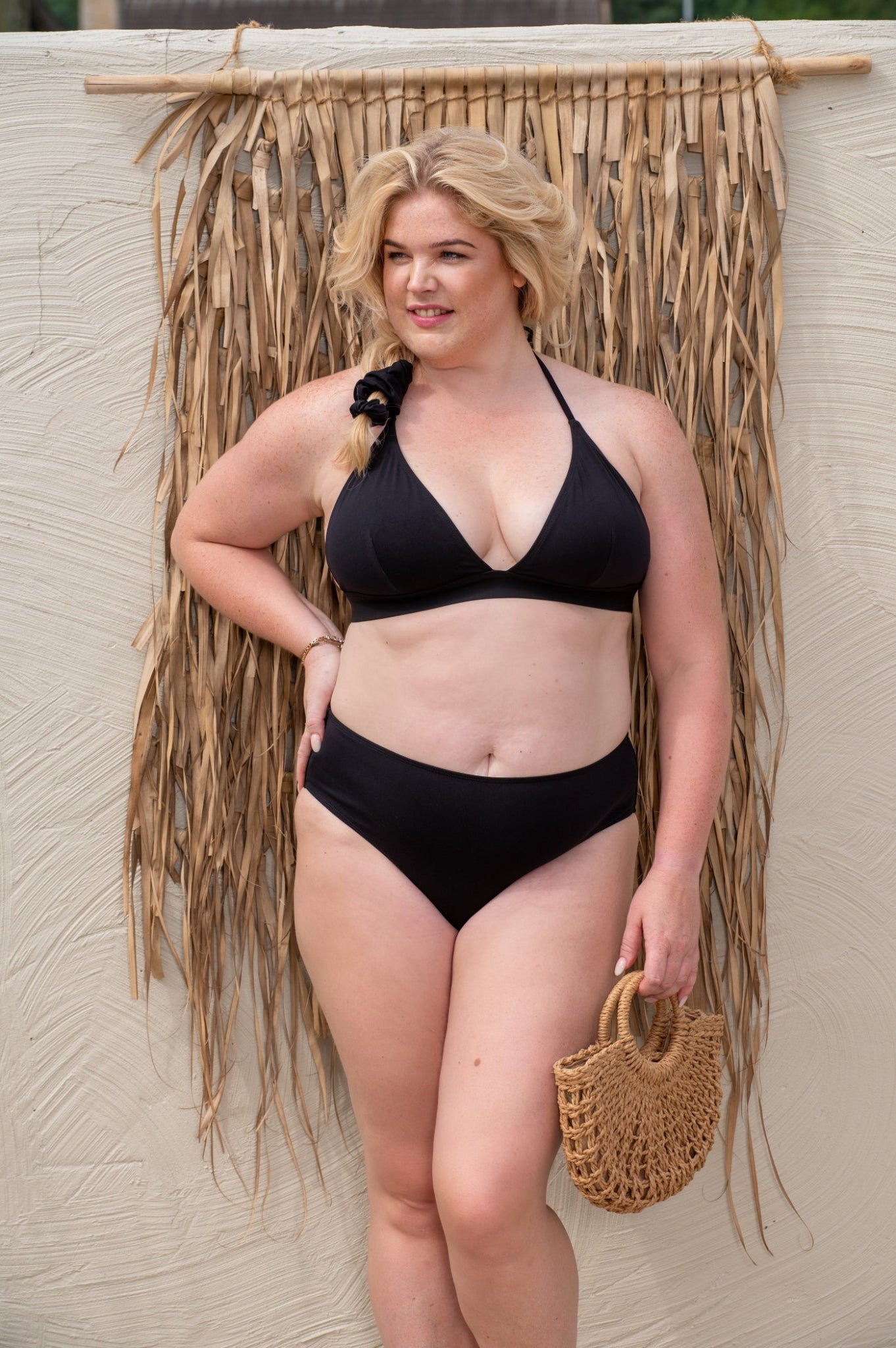 curvy woman wearing a black bikini against a beige background