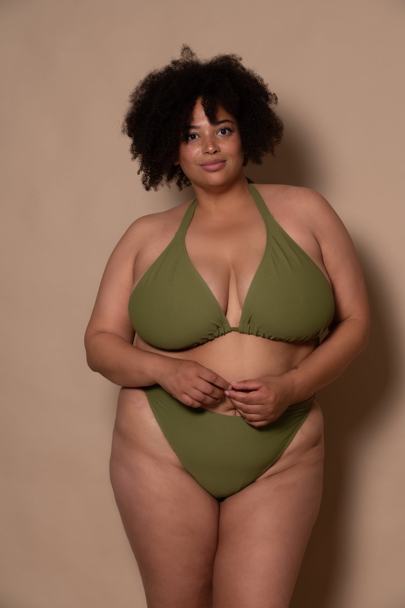 plussize woman wearing a green khaki bikini set against a beige background