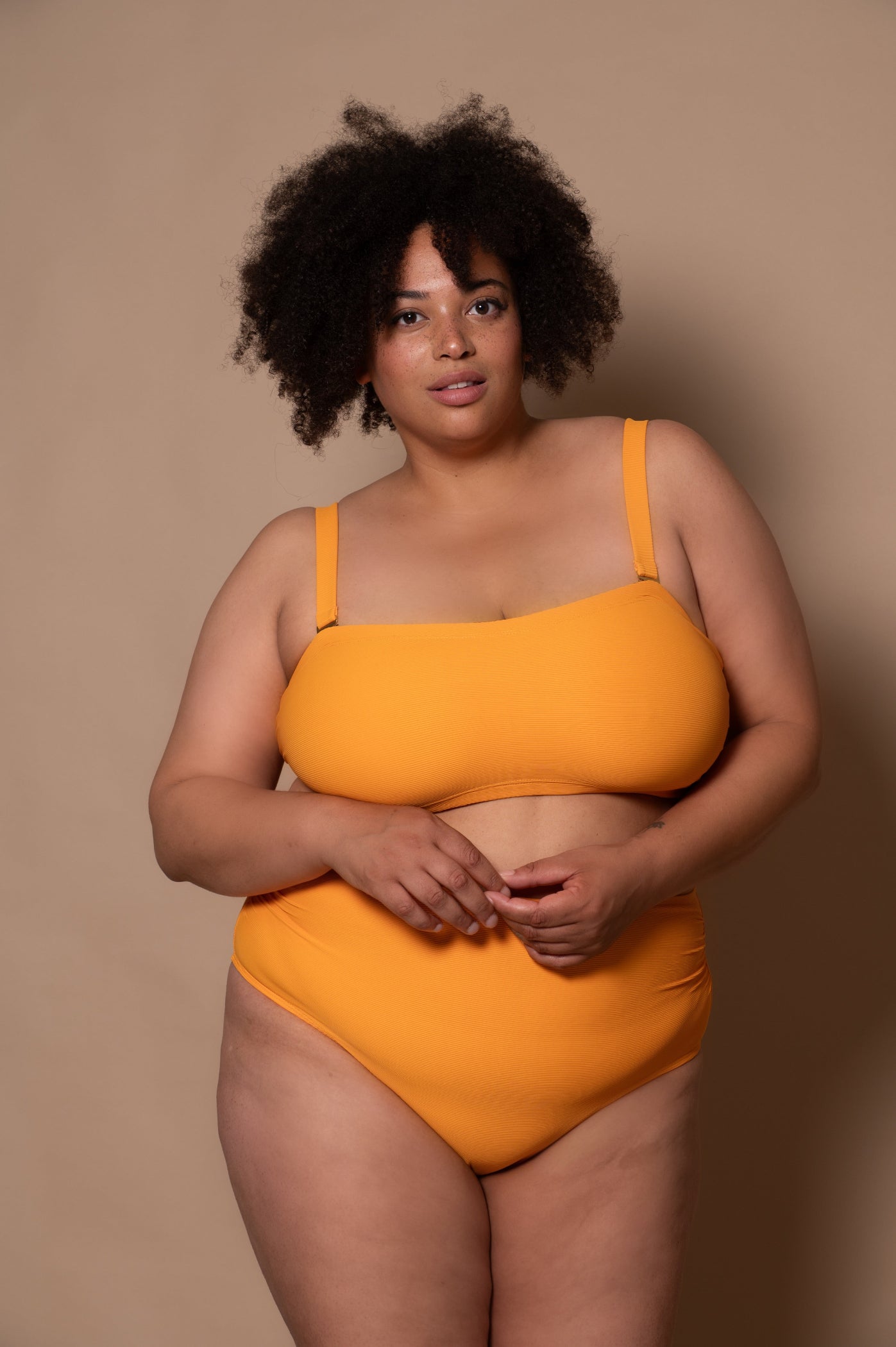 plussize woman wearing a yellow bikini against a beige background