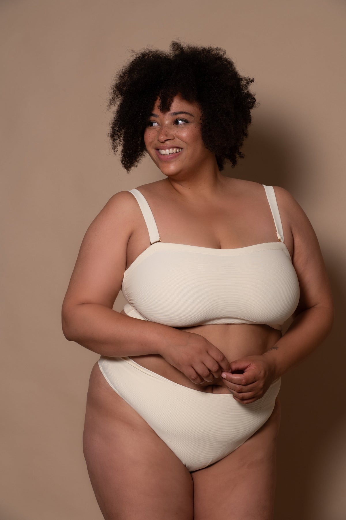 plussize woman wearing a white cream bikini against a beige background
