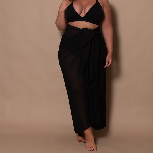 plussize woman wearing a black bikini top and a black sarong against a brown background