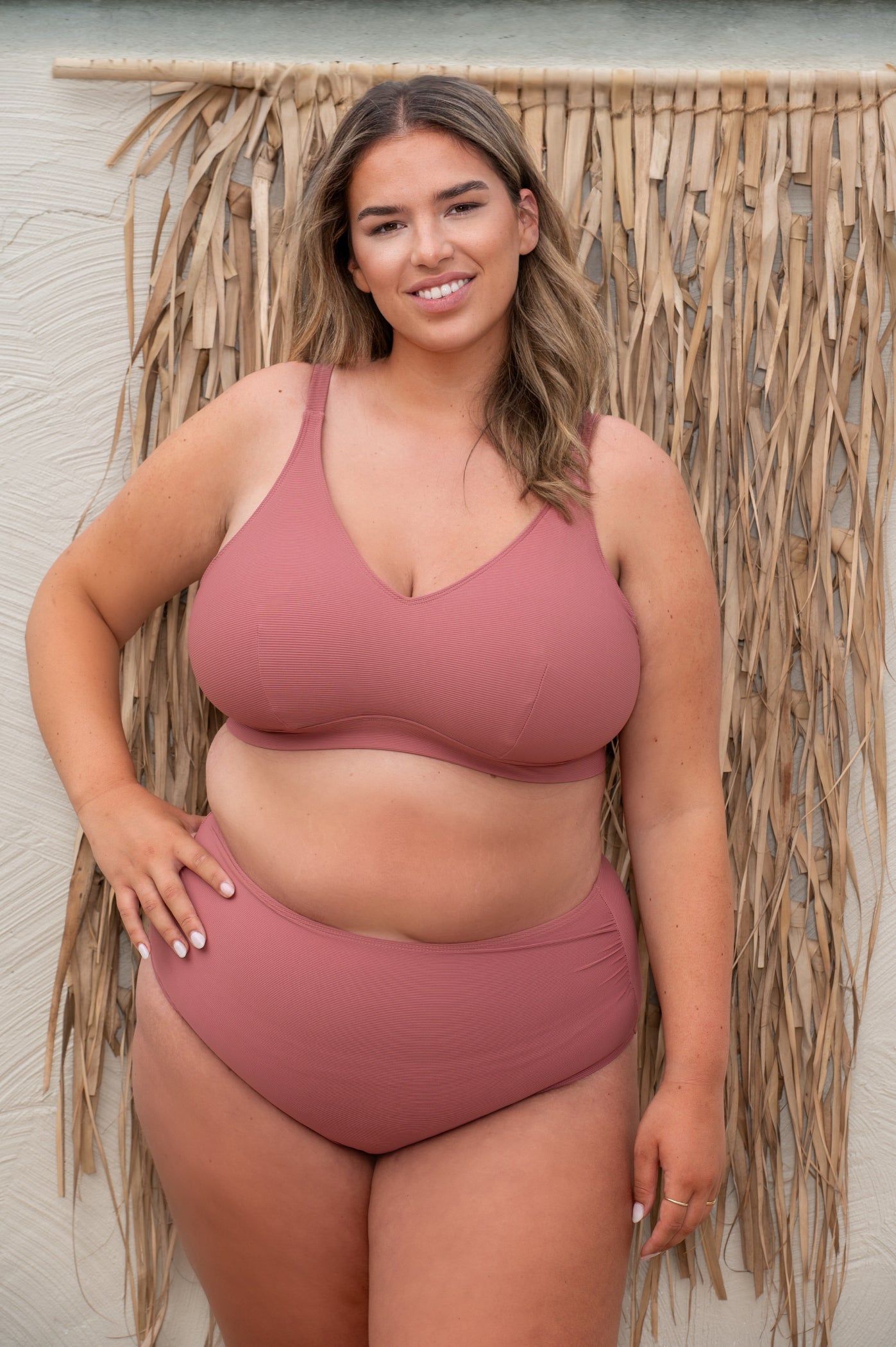 plussize woman wearing a rosewood pink bikini against a beige background