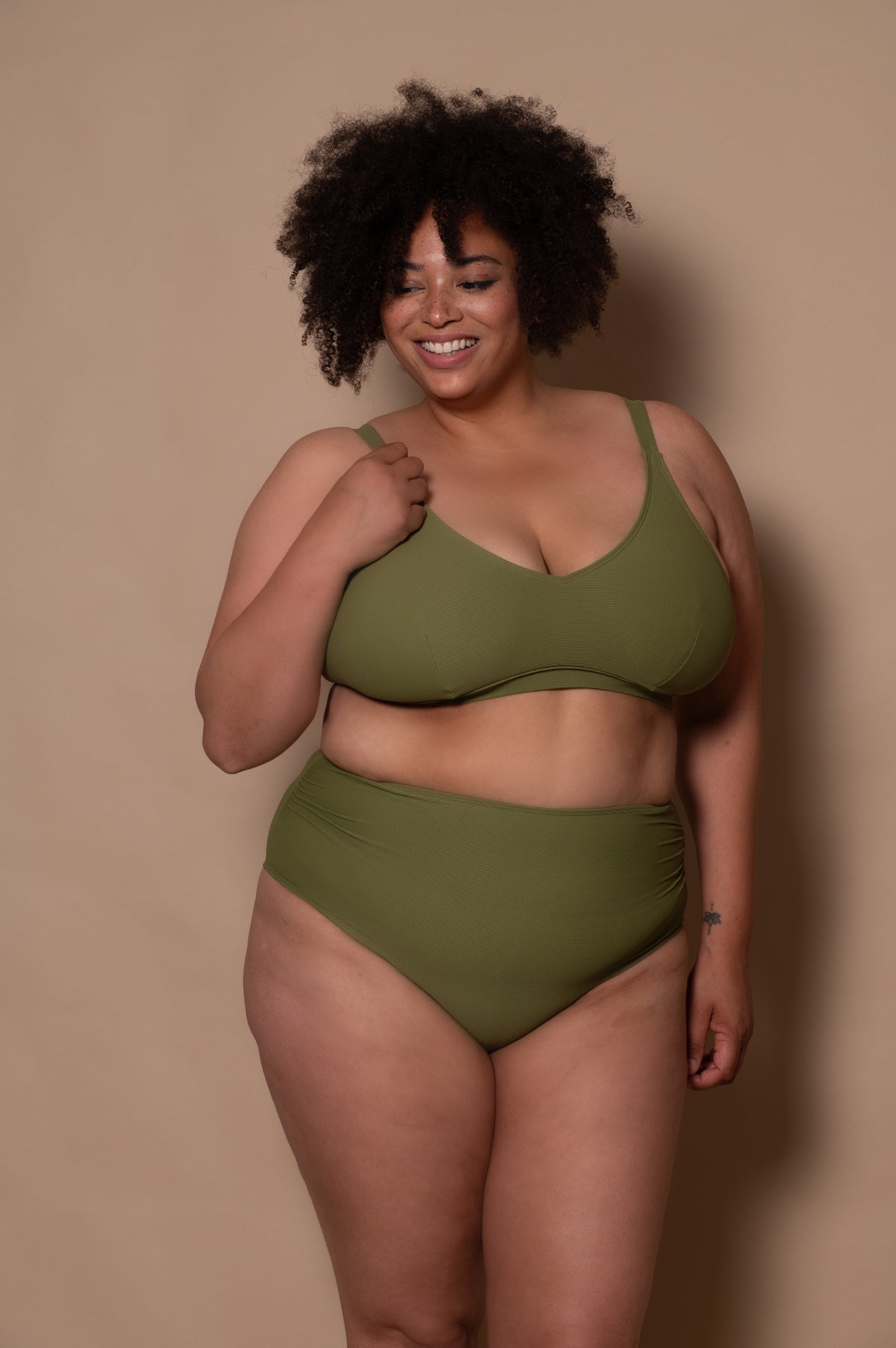 plussize woman wearing a khaki green bikini against a beige background