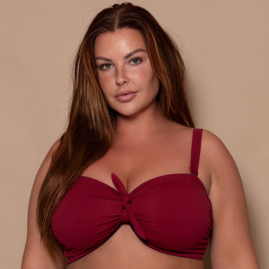 plussize woman wearing a pomegranate red bikini against a beige background