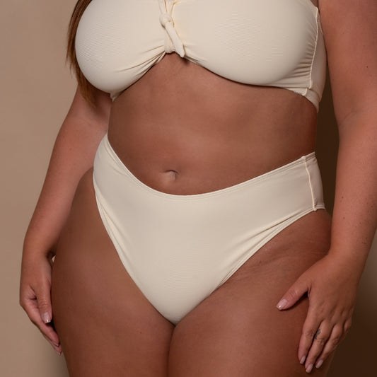 plussize woman wearing a cream white bikini against a beige background