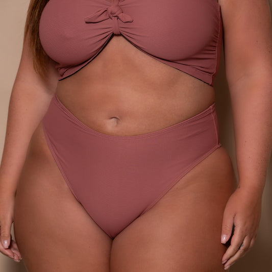 plussize woman wearing a rosewood pink briefs bikini against a beige background