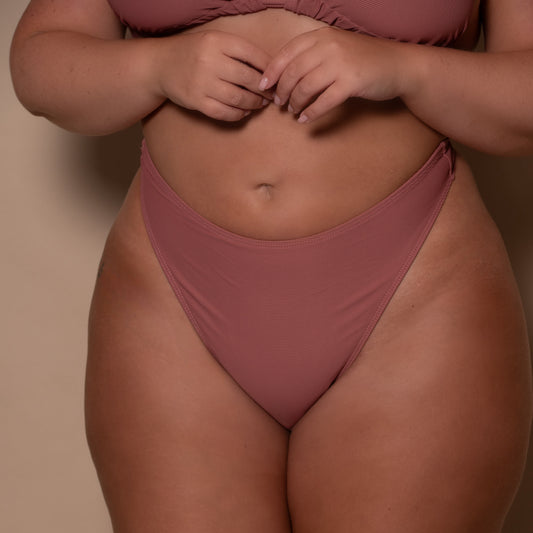 plussize woman wearing a rosewood pink thong bikini against a beige background