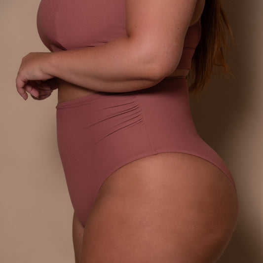 plussize woman wearing a rosewood pink high waist bikini against a beige background
