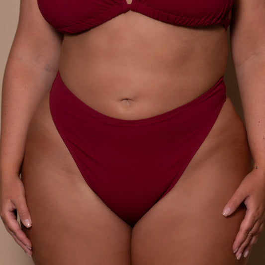 plussize woman wearing a pomegranate red bikini against a beige background