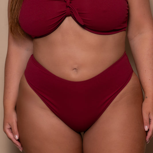 plussize woman wearing a pomegranate red bikini against a beige background