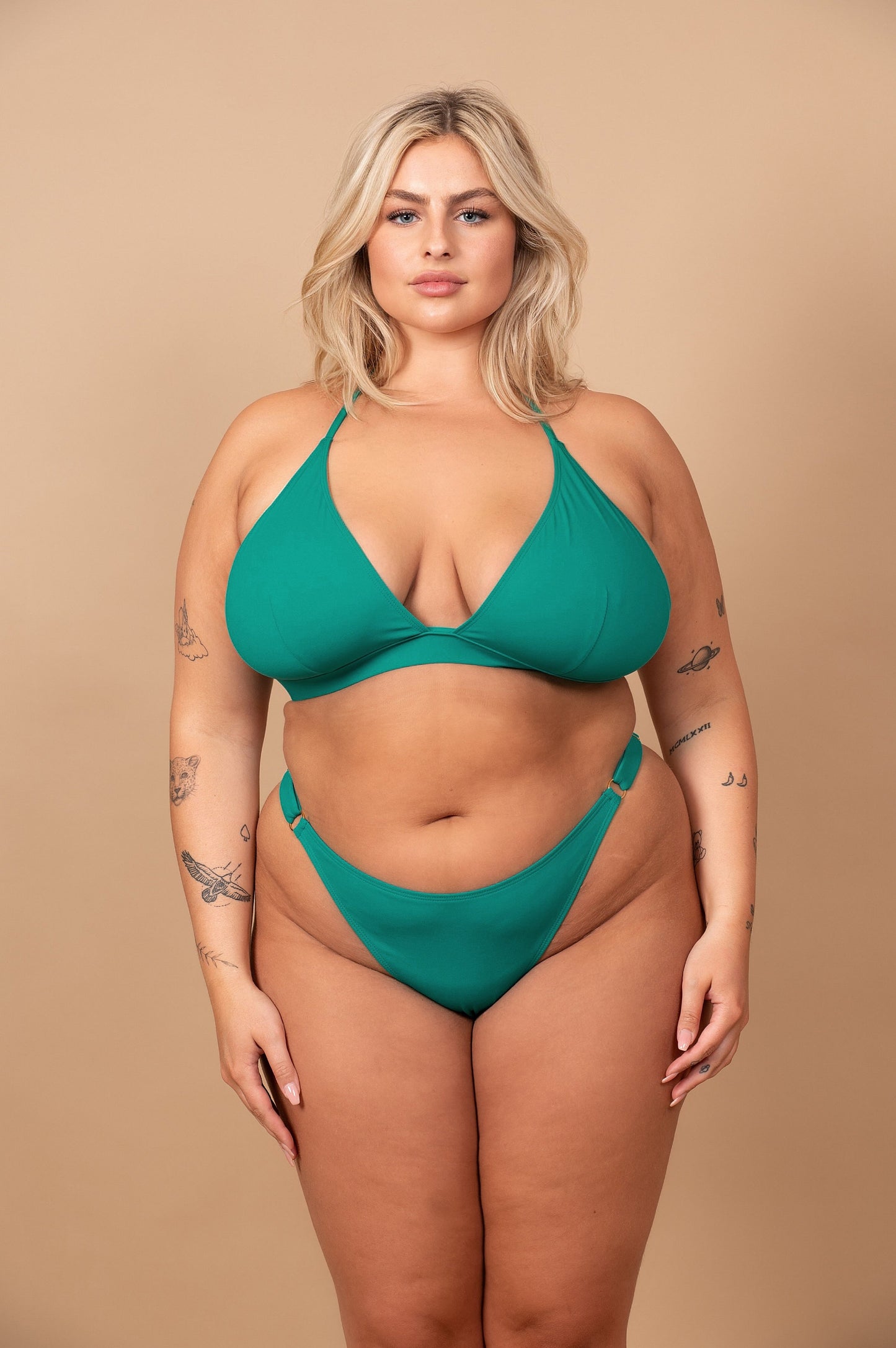 Curvy woman wearing an emerald green bikini against a beige background