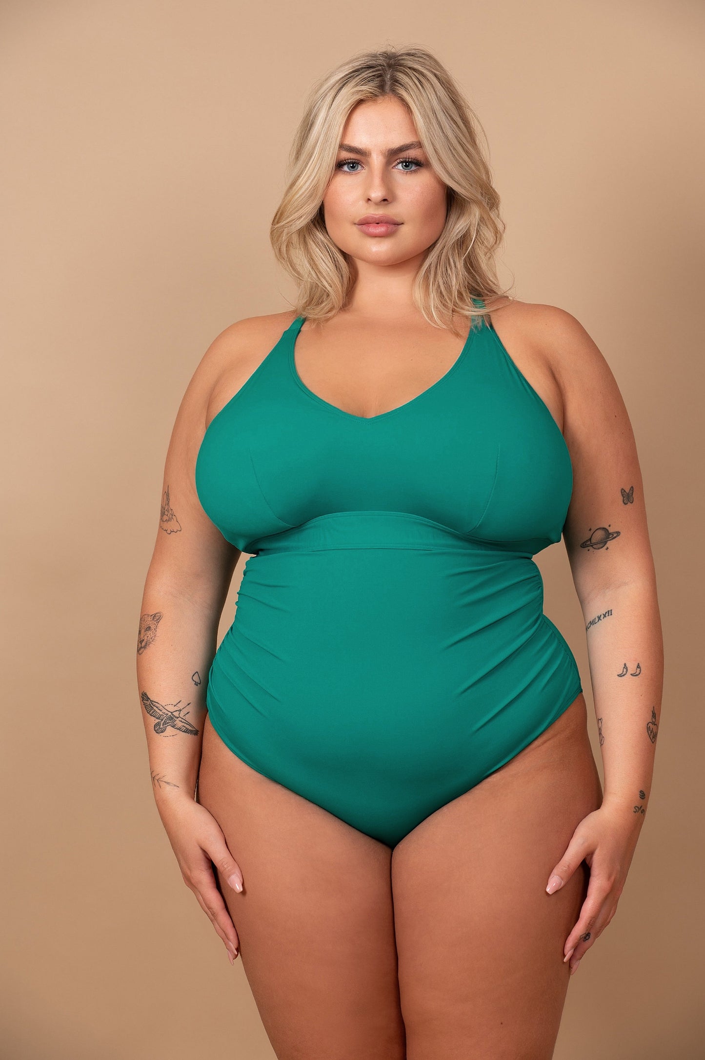 Curvy Woman wearing an emerald green swimsuit against a beige background