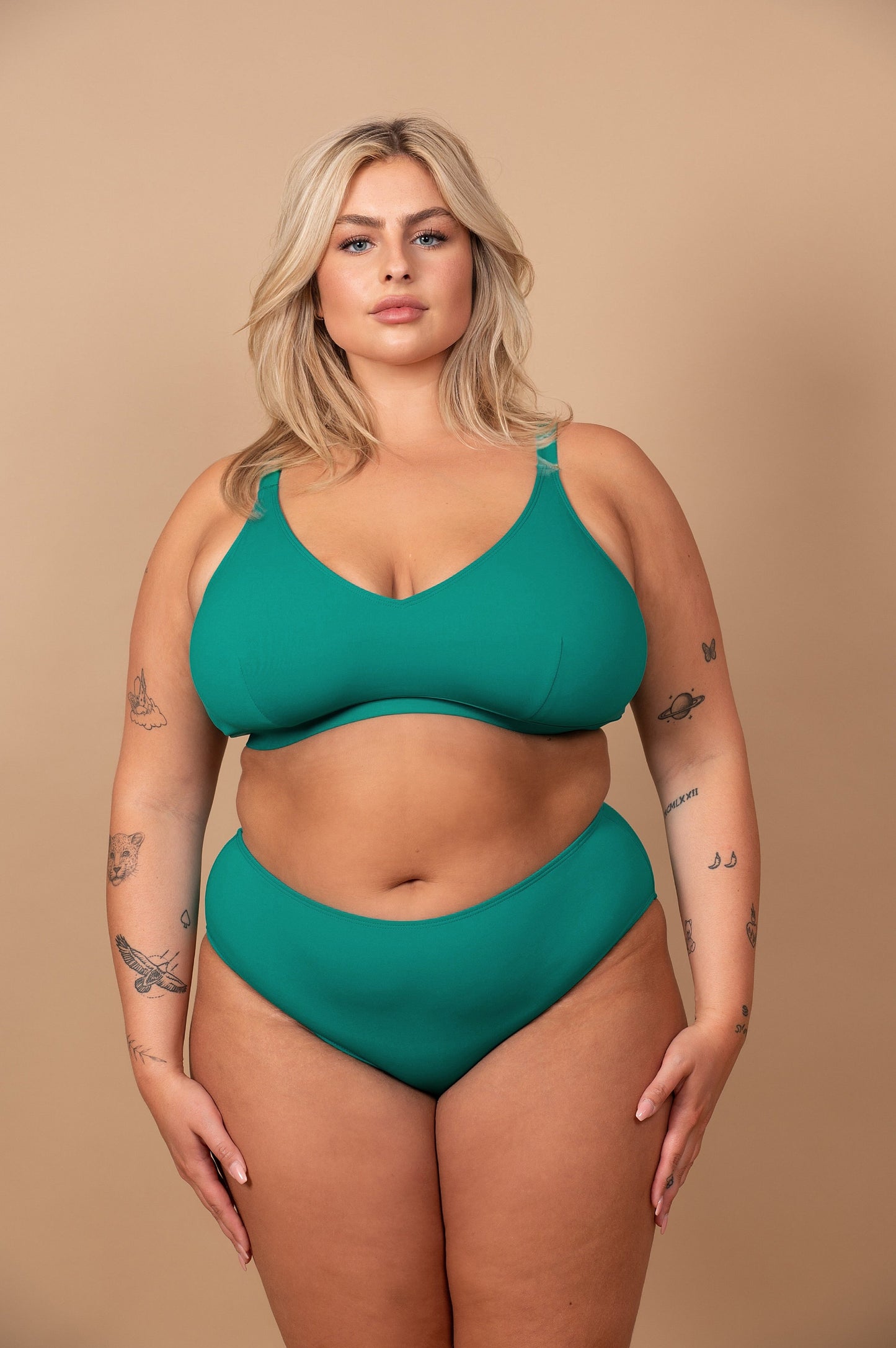 Curvy woman wearing an emerald green bikini against a beige background