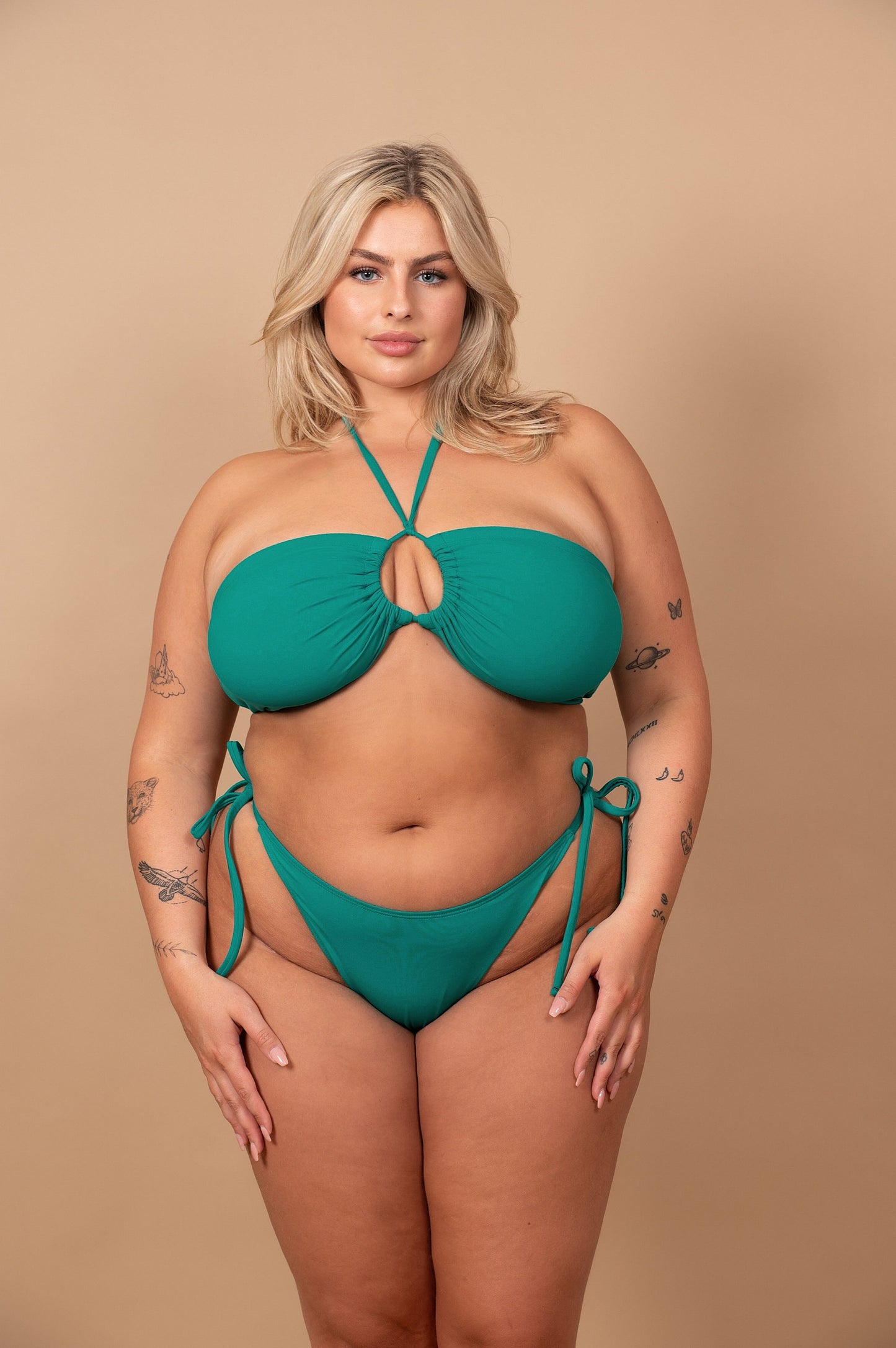 Curvy woman wearing an emerald green bikini against a beige background