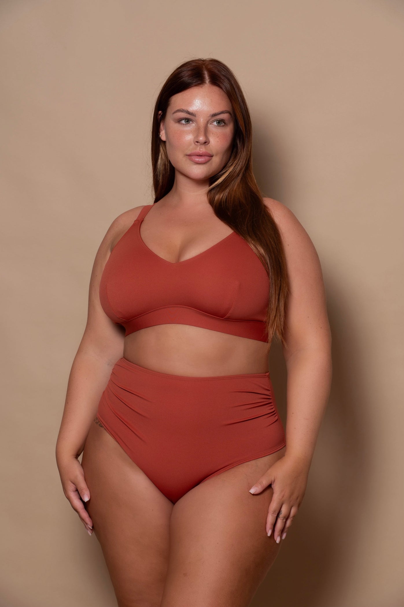 Woman wearing a rust-colored bikini against a beige background