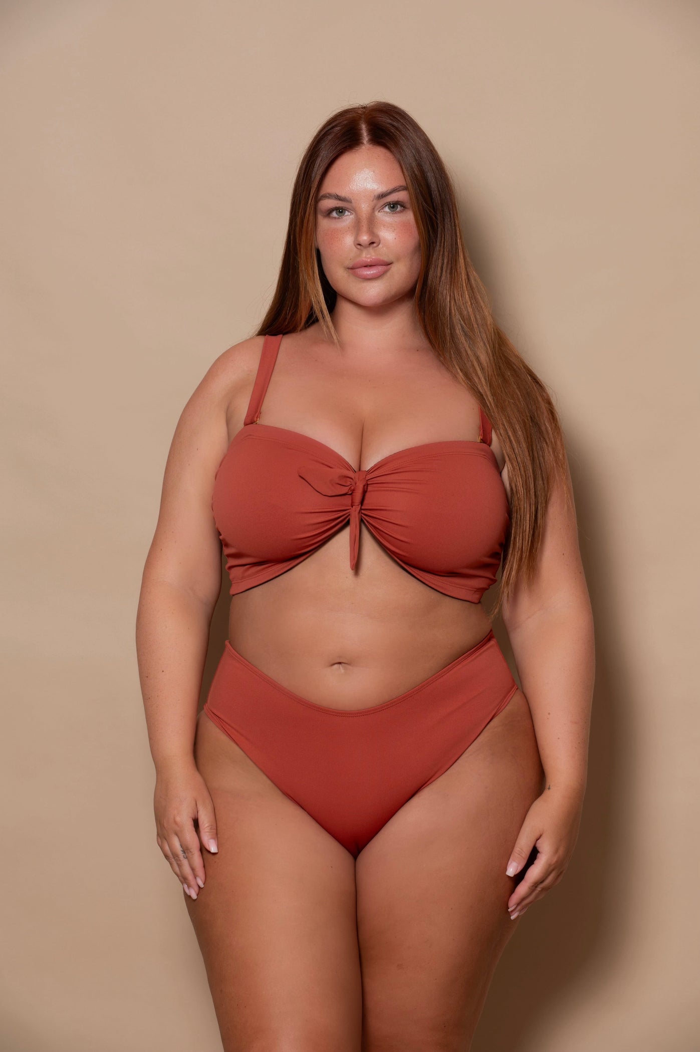 plussize woman wearing a rust red bikini set against a beige background