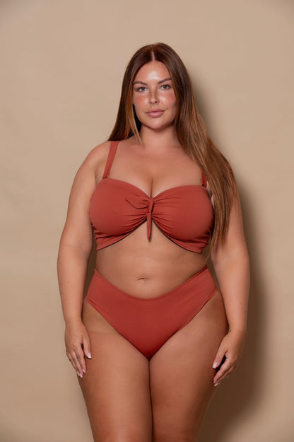 plussize woman wearing a rust red bikini set against a beige background