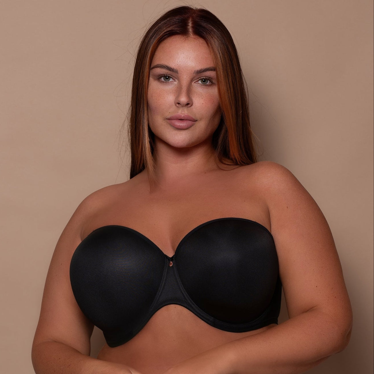 curvy woman wearing a black strapless bra on a beige background
