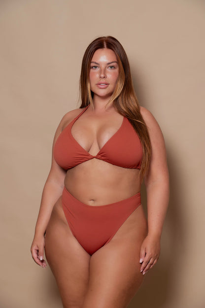plussize woman wearing a rust red bikini set against a beige background