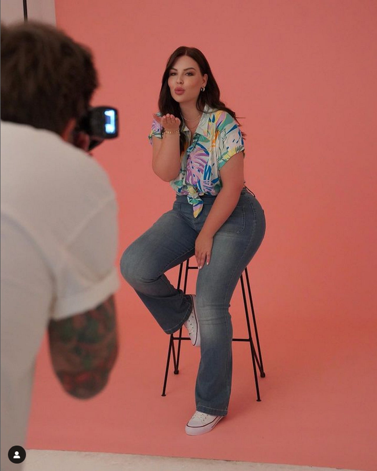 Woman sitting on a stool being photographed against a pink background