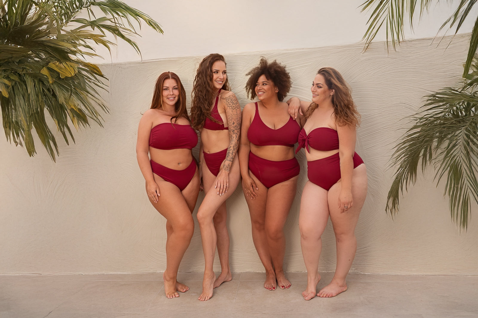Four women wearing red swimsuits standing against a white wall with plants on either side.