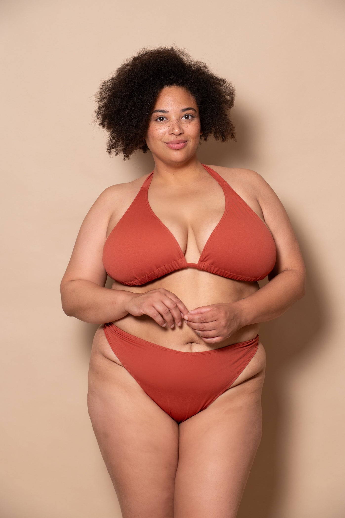 plussize woman wearing a rust red bikini set against a beige background