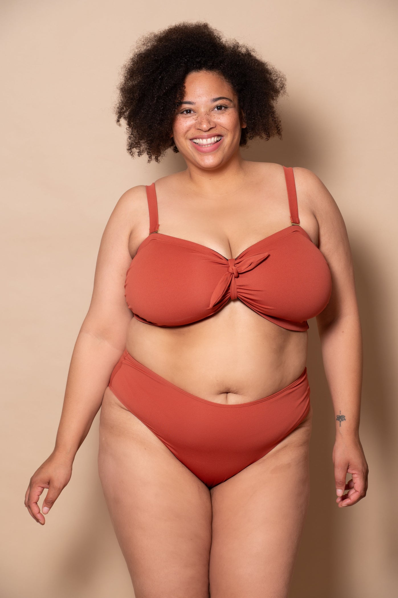 plussize woman wearing a rust red bikini set against a beige background