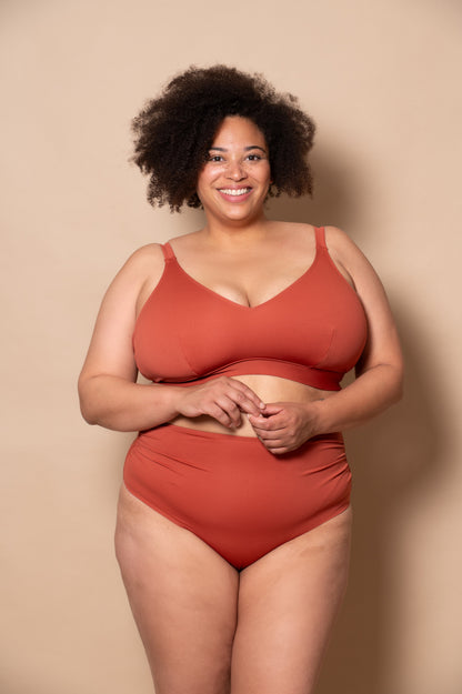 plussize woman wearing a rust-colored bikini against a beige background