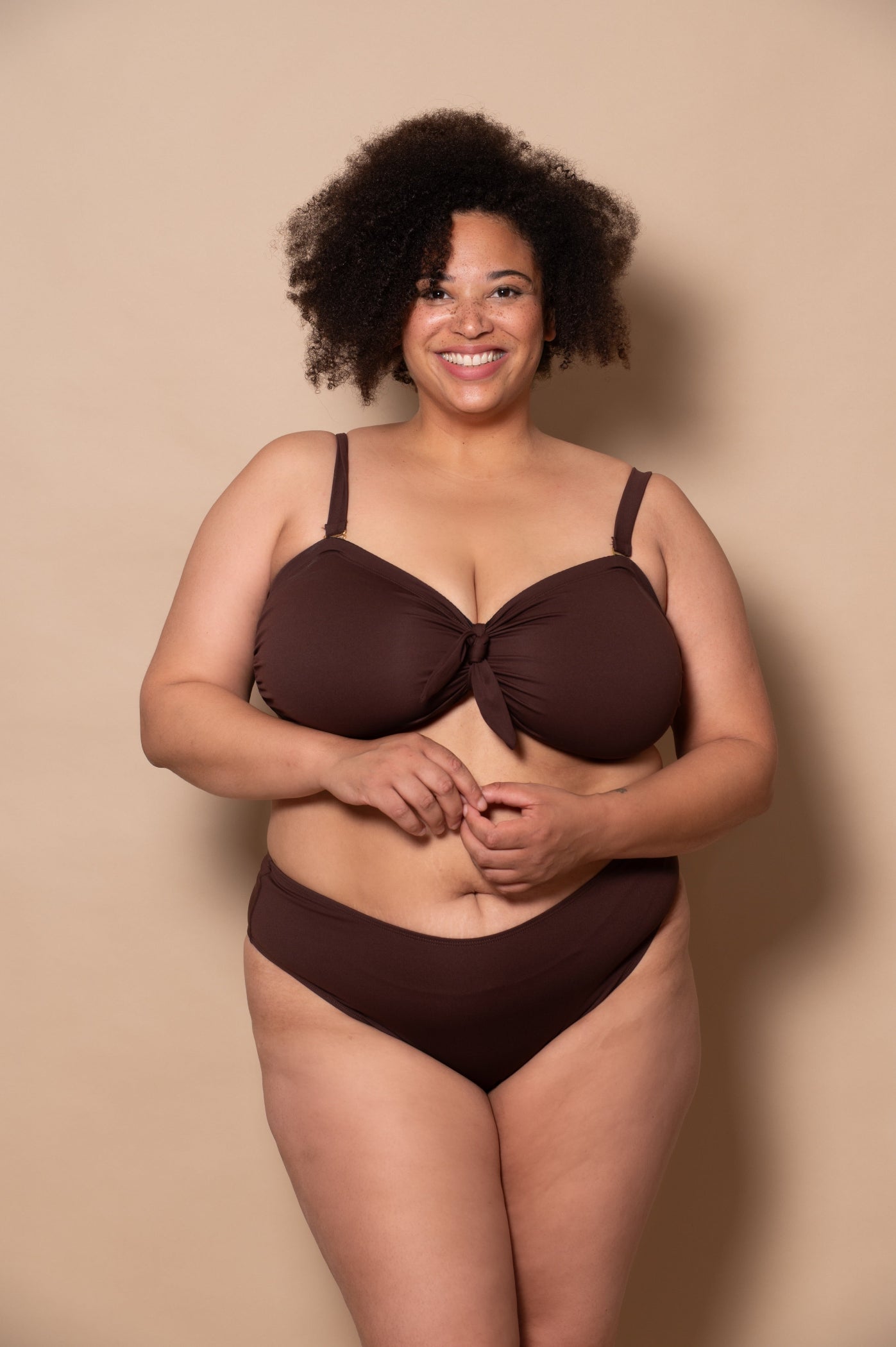 plussize woman wearing a chocolate brown bikini against a beige background