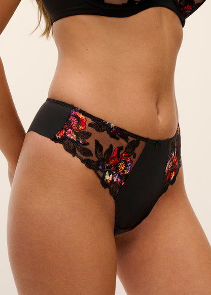 woman wearing a black thong with black lace and embroidered flower details in sunset colors