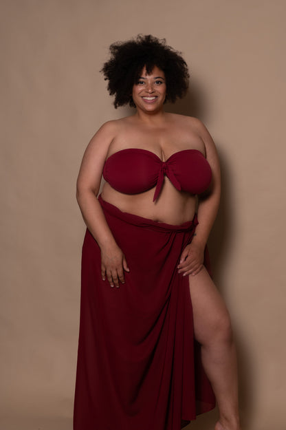 plussize woman wearing a wine red bikini and pareo cover up against a beige background