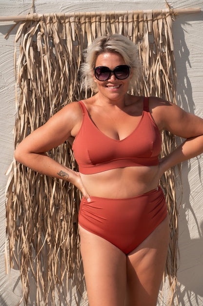 woman wearing a rust red bikini  against a beige background