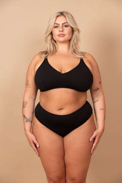 curvy woman wearing a black bikini against a beige background