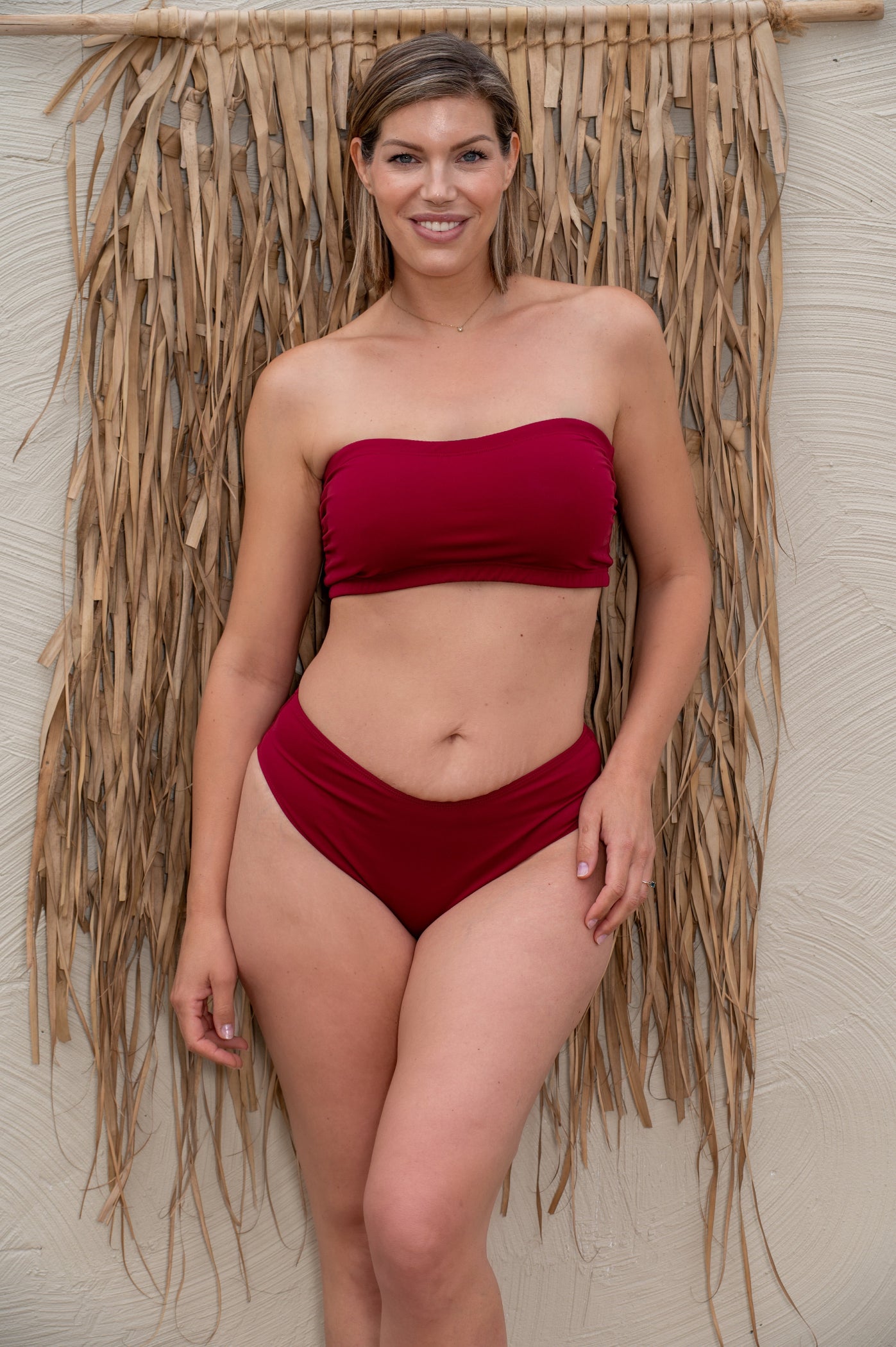 Woman wearing a wine red bikini standing against a textured wall.
