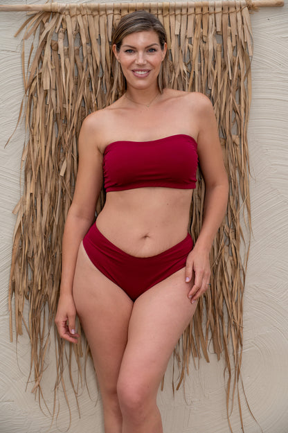 Woman wearing a wine red bikini standing against a textured wall.
