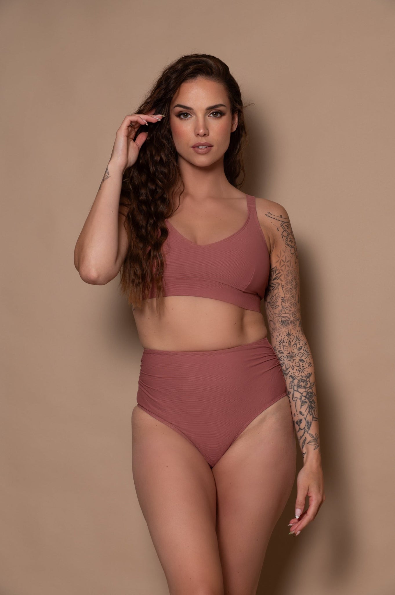 Woman wearing a rosewood - pink bikini against a beige background