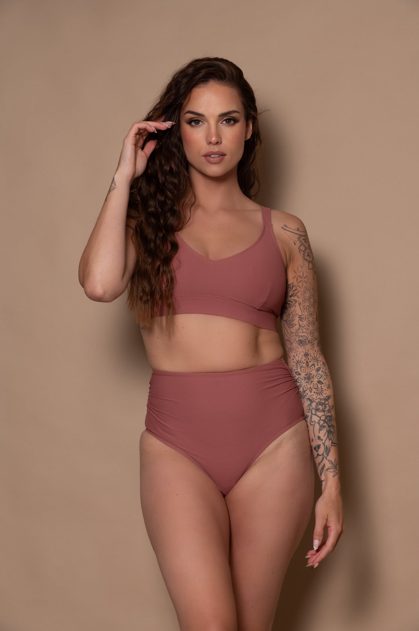 woman wearing a rosewood pink bikini  against a beige background