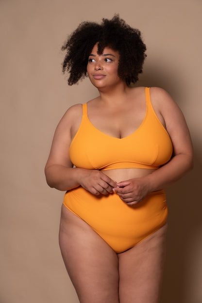 plussize woman wearing a yellow bikini against a beige background