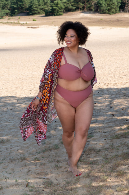 plussize woman in a pink bikini and colorful cover-up walking on a sandy beach.