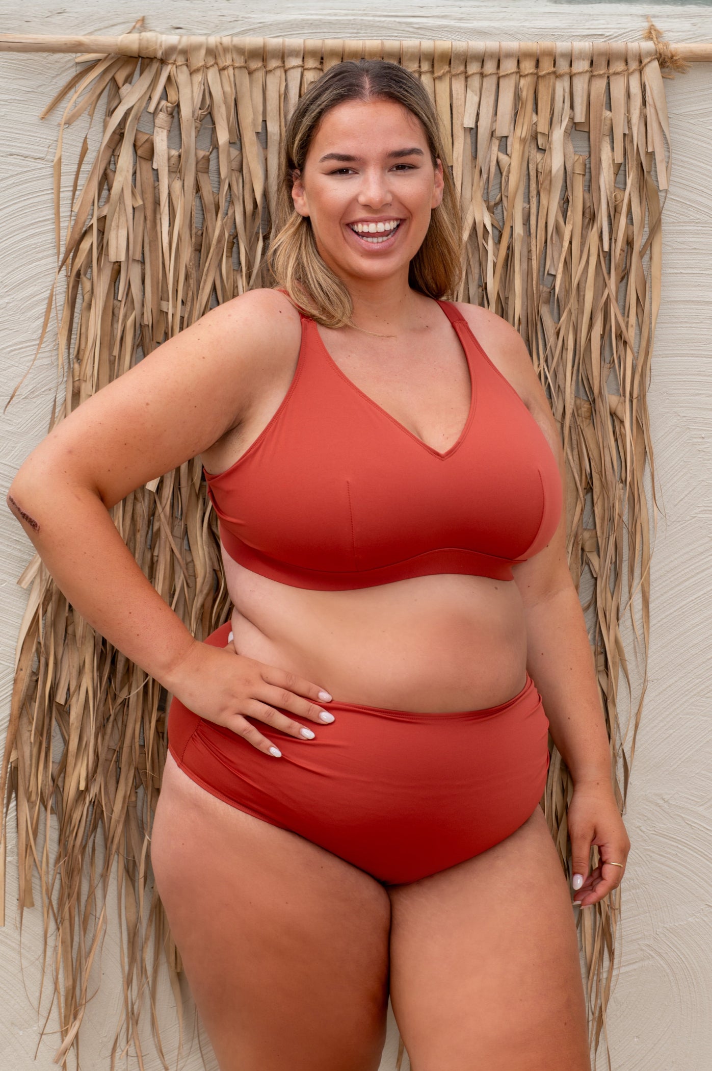 plussize woman wearing a rust red bikini  against a beige background