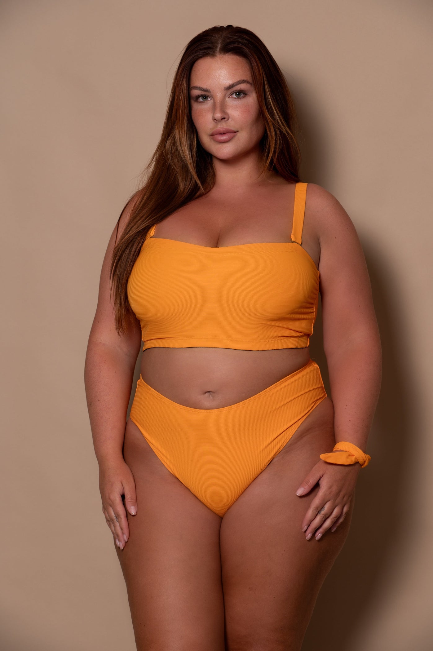plussize woman wearing a yellow sunflower bikini against a beige background