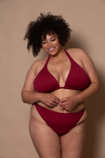 plussize woman wearing a wine red bikini  against a beige background