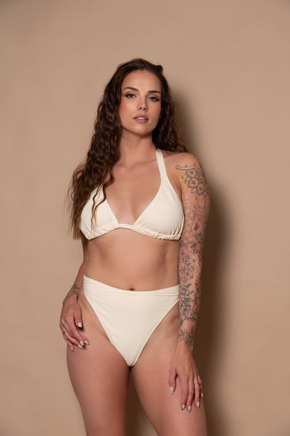 woman wearing a white cream bikini against a beige background